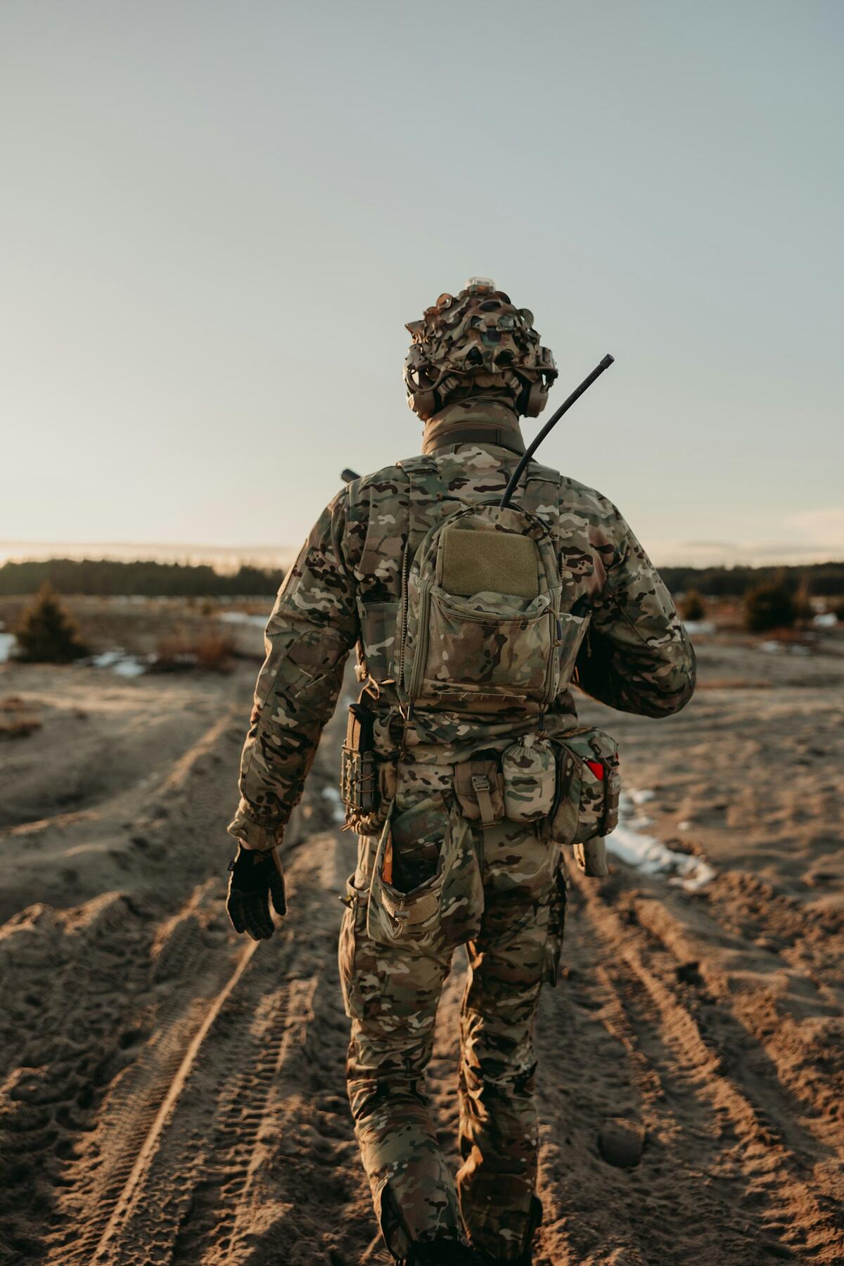 A soldier with a pack walks away down a dusty track at first light