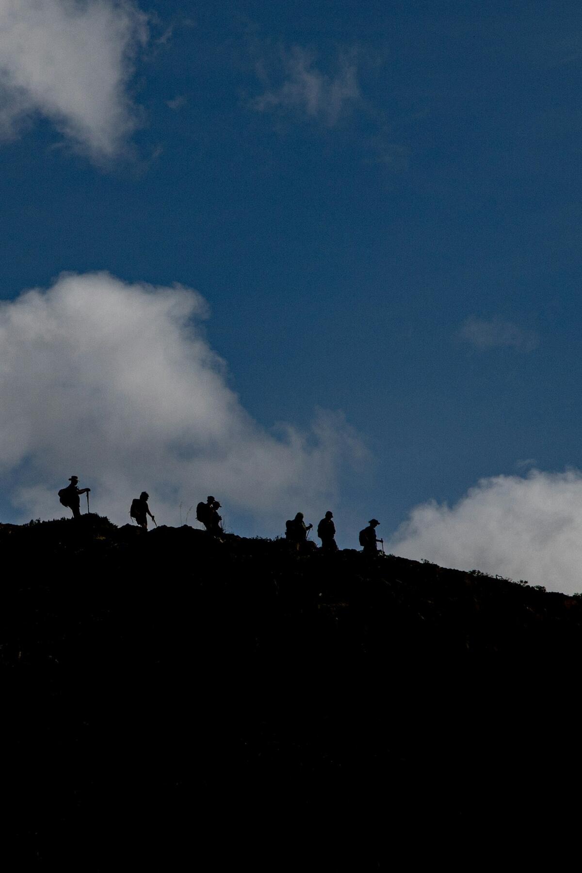 Silhouetted hikers climb a mountain ridge under a cloudy sky